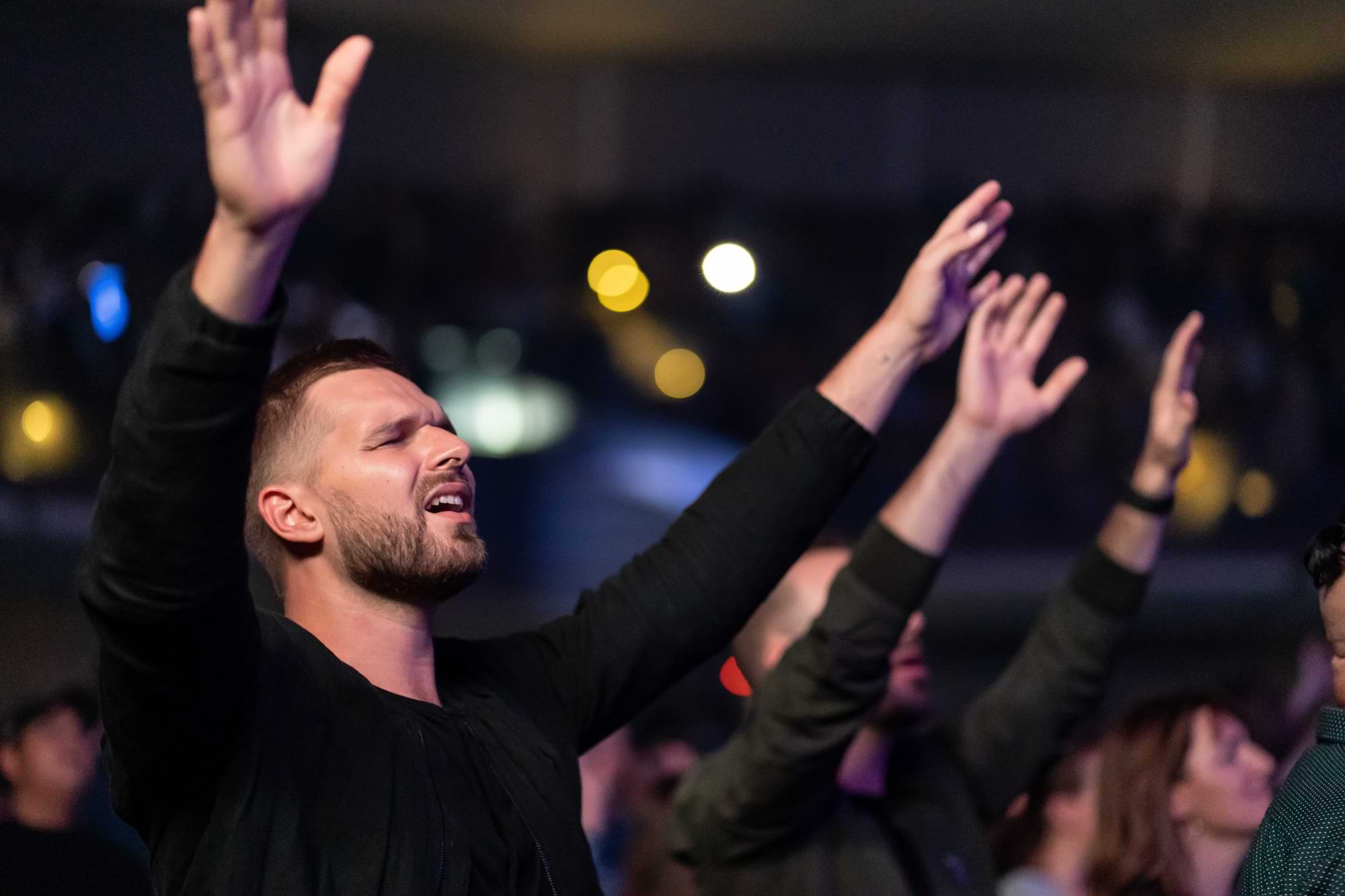 Man with hands up and eyes closed in a crowd